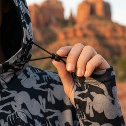 Person wearing a black and white jackalope patterned jacket with a blurred desert landscape in the background