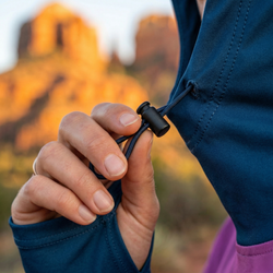 Person adjusting a cord on a blue jacket with a blurred natural background