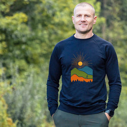 Man wearing a navy blue sweatshirt with a colorful mountain design outdoors.