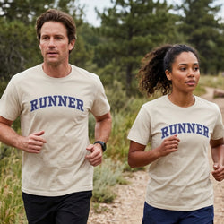 A man and a woman jogging outdoors on a dirt path, both wearing matching beige short-sleeve T-shirts with 'RUNNER' printed across the chest in dark blue.
