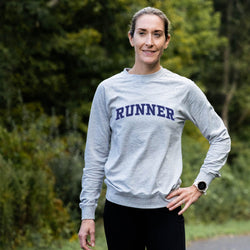 Woman wearing a gray sweatshirt with 'RUNNER' printed on it, standing outdoors.