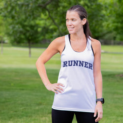 Woman wearing a white tank top with 'RUNNER' printed on it, standing outdoors.