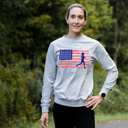 Woman wearing a gray sweatshirt with an American flag and running figure design, standing outdoors.