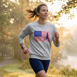 Woman running outdoors wearing a sweatshirt with an American flag and running person graphic.