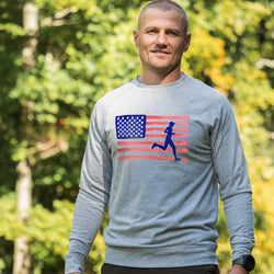 Man wearing a gray long-sleeve shirt with an American flag and running person graphic outdoors.
