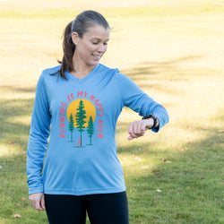 Woman wearing a blue long-sleeve shirt with a nature-themed running design outdoors.