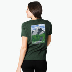 Person wearing a green t-shirt with a mountain graphic on the back, standing against a white background