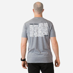 Person wearing a gray t-shirt with running text on the back, standing against a white background
