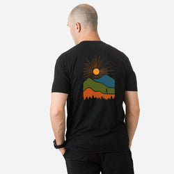 Person wearing a black t-shirt with a colorful mountain graphic on the back against a white background