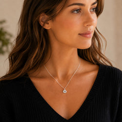 A woman wearing a delicate silver pendant necklace with a 10K engraved, styled with a black ribbed V-neck top.