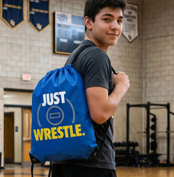 Person wearing a blue 'Just Wrestle' backpack in a gymnasium.