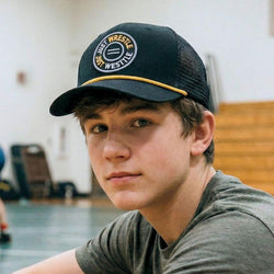 Person wearing a cap with a wrestling logo in an indoor setting