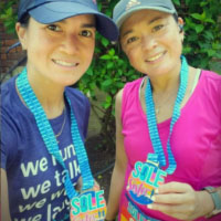 Two runners wearing purple and pink shirts with colorful Sole Sister virtual race medals and visors