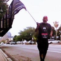 Runner in black t-shirt and red headband carrying a thin blue line flag during a virtual race
