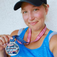 Runner in blue tank top and black hat holding a patriotic "We Run Free" virtual race medal