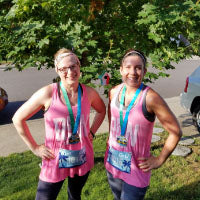 Two runners wearing pink tank tops with matching virtual race medals and tropical themed bibs