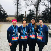Four runners wearing navy Sole Sister shirts with matching virtual race medals and colorful bibs