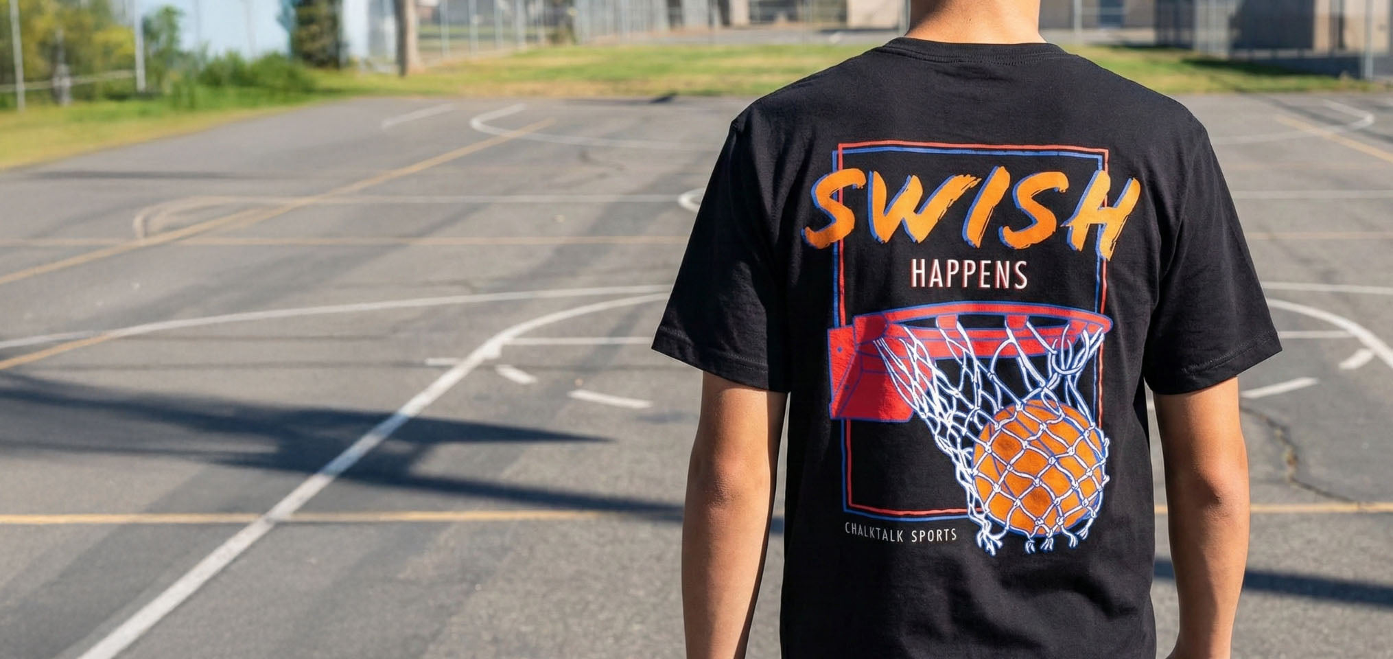 Boy wearing a black basketball t-shirt featuring Swish Happens slogan and ball in net graphic on the back.