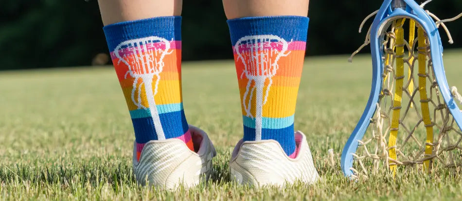 Person wearing colorful lacrosse-themed socks on a grassy field with a lacrosse stick