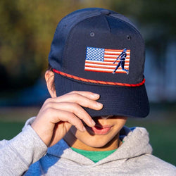 Boy wearing a navy blue baseball rope hat featuring an embroidered American flag and batter silhouette.