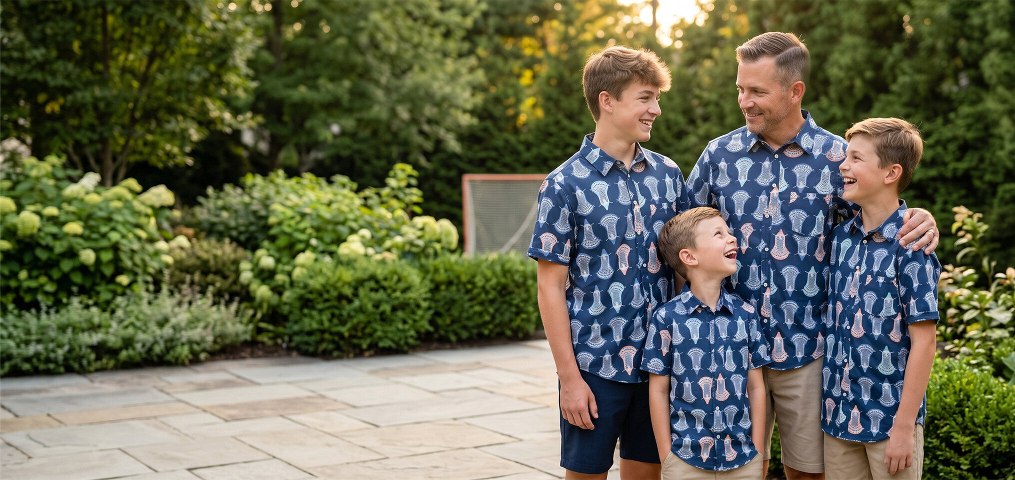Family of four wearing matching blue lacrosse patterned polo shirts standing outdoors in a garden.