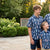 Family of four wearing matching blue lacrosse patterned button downs standing outdoors in a garden.