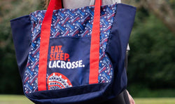 Navy lacrosse tote bag with red straps and "EAT. SLEEP. LACROSSE." text with a lacrosse head and stick pattern.