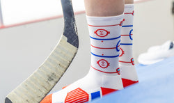 White hockey socks featuring a red and blue ice rink diagram pattern worn next to a hockey stick.