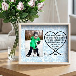 Framed photo of a child with hockey equipment and a heart-shaped mothers day message, next to a vase of flowers.