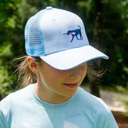 Girl wearing light blue lacrosse trucker hat featuring an embroidered dog holding a stick graphic.