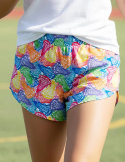 Model wearing girls lacrosse shorts featuring a colorful multi-colored stick head pattern.
