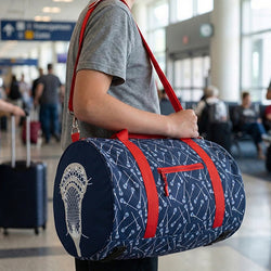 Person holding a blue lacrosse duffel bag with red straps in an airport setting