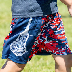 Youth wearing patriotic camo lacrosse-themed shorts on a grassy background