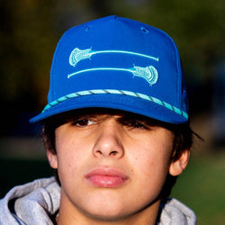 Boy wearing blue lacrosse rope hat featuring embroidered white lacrosse sticks graphic.