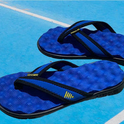 Blue recovery flip-flops featuring a textured massage footbed on a blue court.