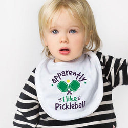 Child wearing a white pickleball baby bib featuring green paddles and Apparently I Like Pickleball text.