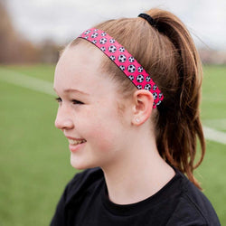 Girl wearing a pink soccer headband featuring a repeating black and white soccer ball pattern.