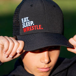Youth wearing black wrestling trucker hat featuring embroidered Eat Sleep Wrestle slogan.