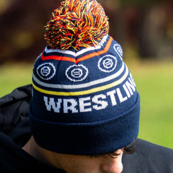 Youth wearing navy blue knit wrestling beanie featuring a multi-colored pom-pom and large Wrestling text.