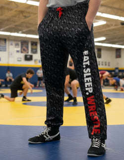 Black wrestling lounge pants featuring vertical Eat Sleep Wrestle text down the leg.