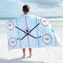 A boy holding a beach towel with hockey rink design on a sandy beach.