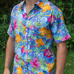 Person wearing a colorful, tropical floral lacrosse patterned button-down shirt, standing on the grass with lush green trees in the background