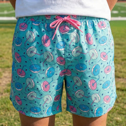 Turquoise athletic Ryder shorts with a pattern of donuts and hockey sticks worn by a person on a grass athletic field