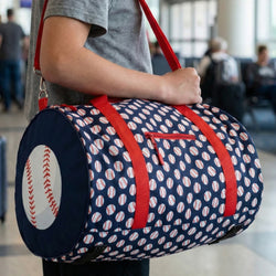 Person holding a navy duffel bag with red straps and baseball pattern, in an airport