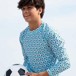 Child wearing a shirt with soccer ball pattern shirt holding a soccer ball against a light background