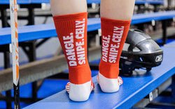 Person wearing red mid-calf hockey crew socks featuring white Dangle Snipe Celly text on back.