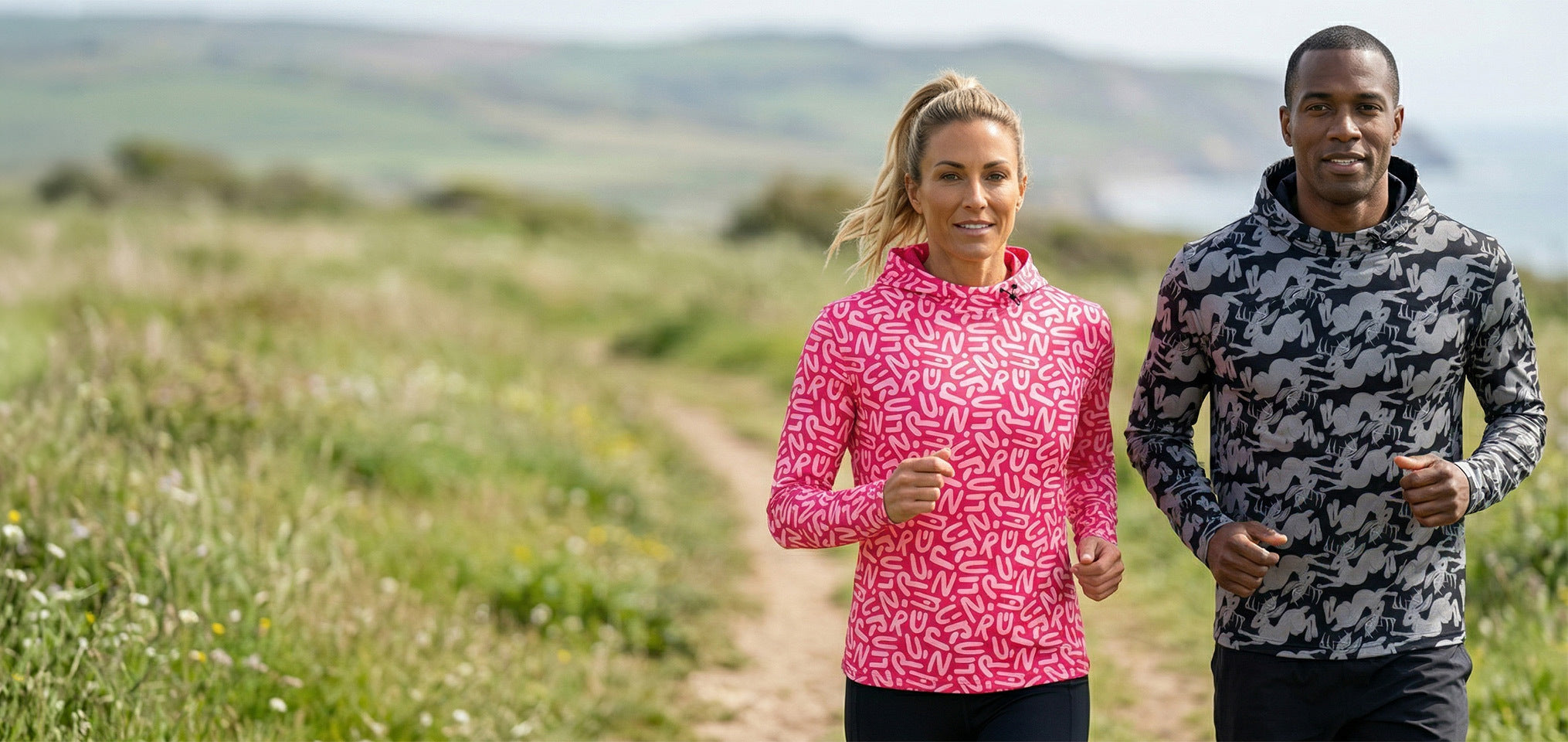 Two people wearing patterned running hoodies outdoors with a scenic background