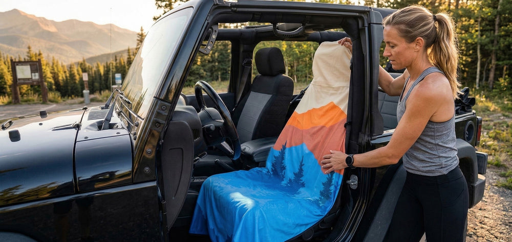 Person setting up a colorful blanket on the back of an open car in a natural setting.