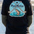 Black graphic t-shirt featuring Pond Hockey Fishing Club design with crossed sticks and trout on frozen lake background.