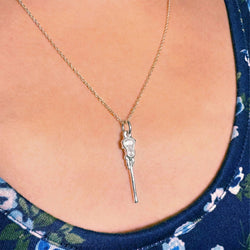 Necklace with a lacrosse stick on a person wearing a blue floral top.